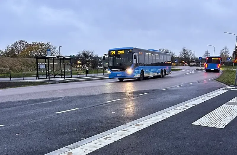 Blå buss som kör på gata med busshållplats