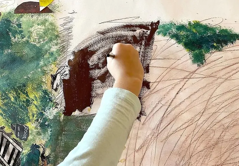 En barnhand tecknar och målar färger på ett vitt papper. 